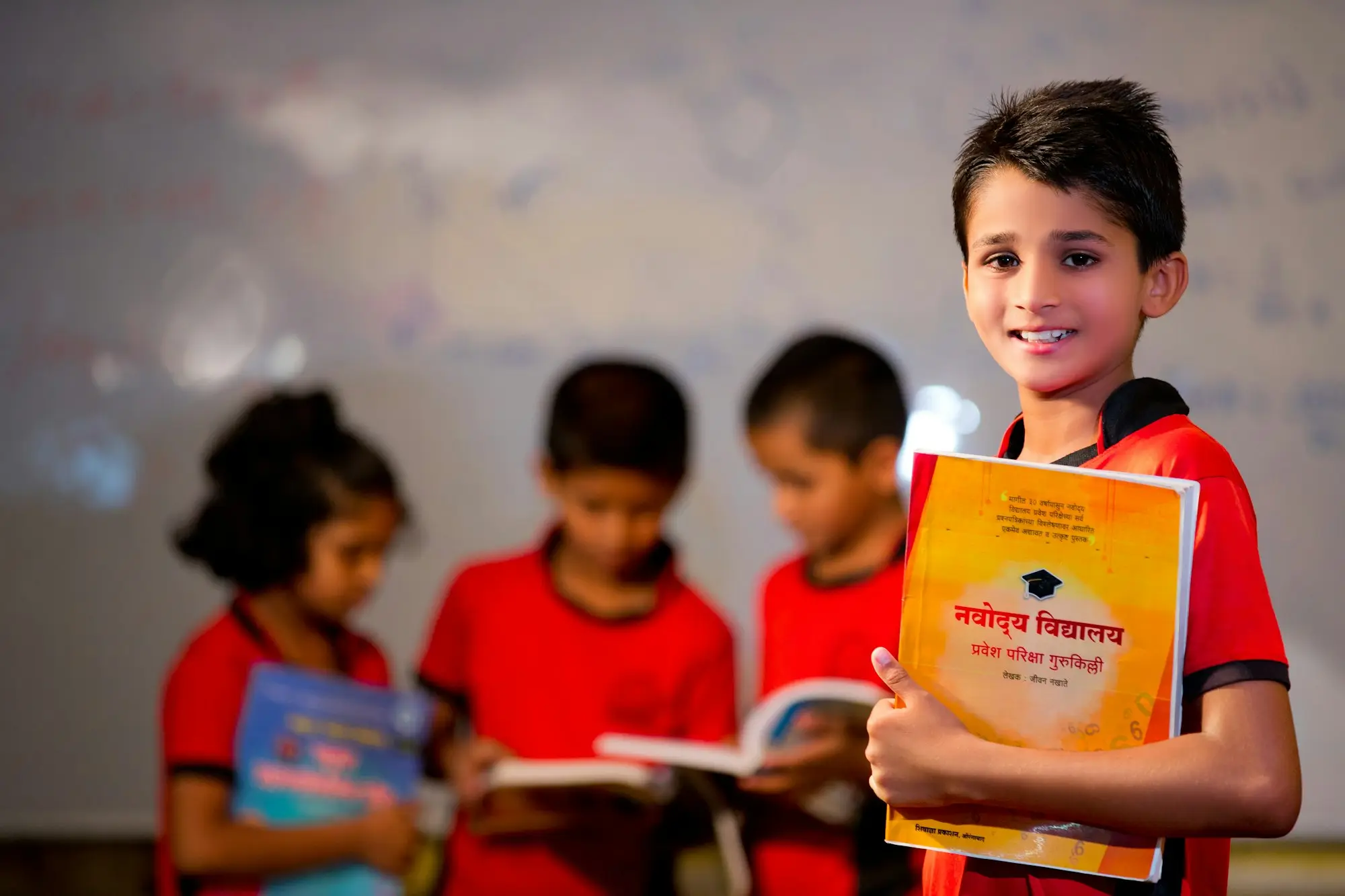 A boy holding a textbook, with other children reading behind him