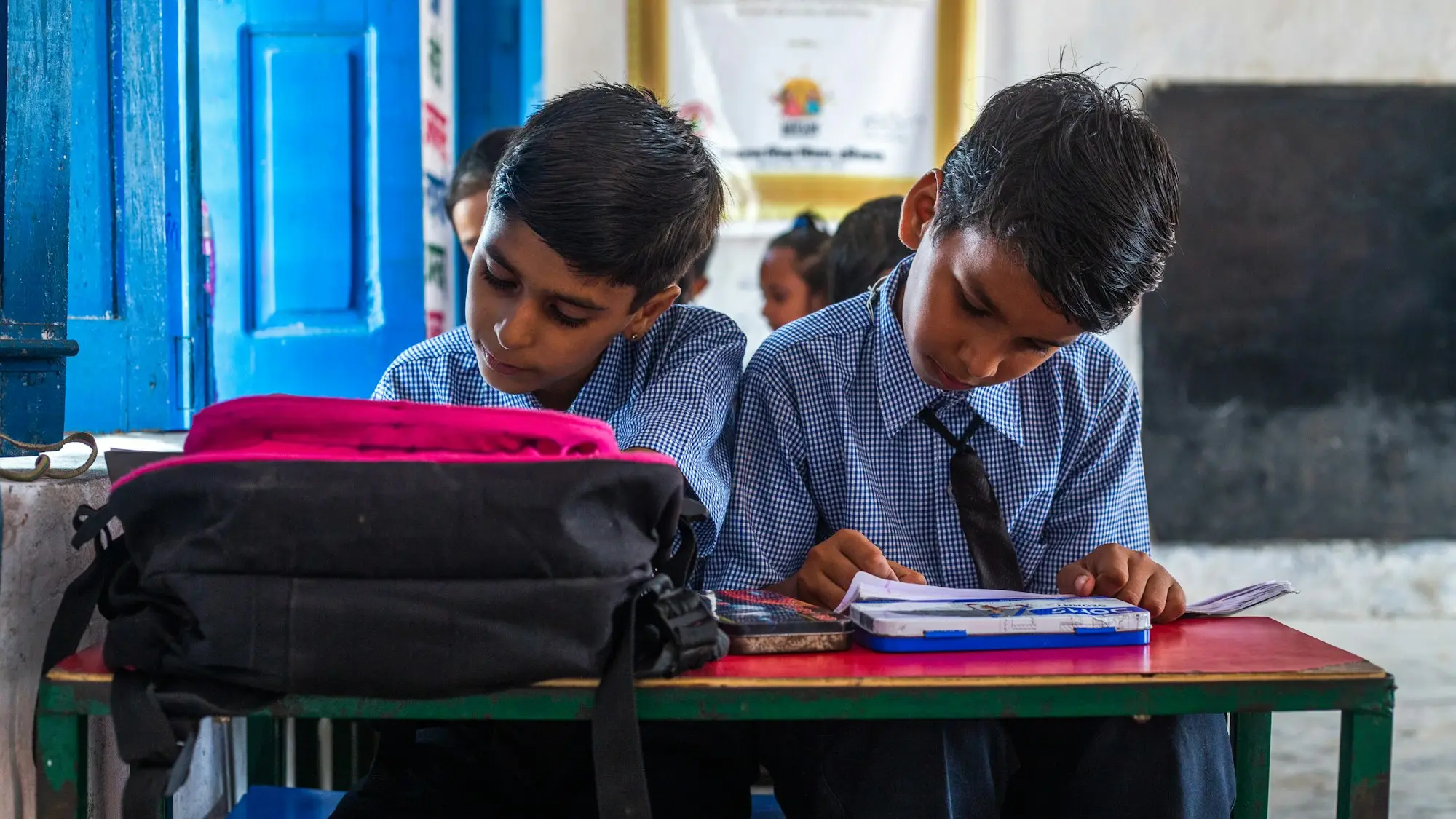 Two boys working at a desk with school bags beside them