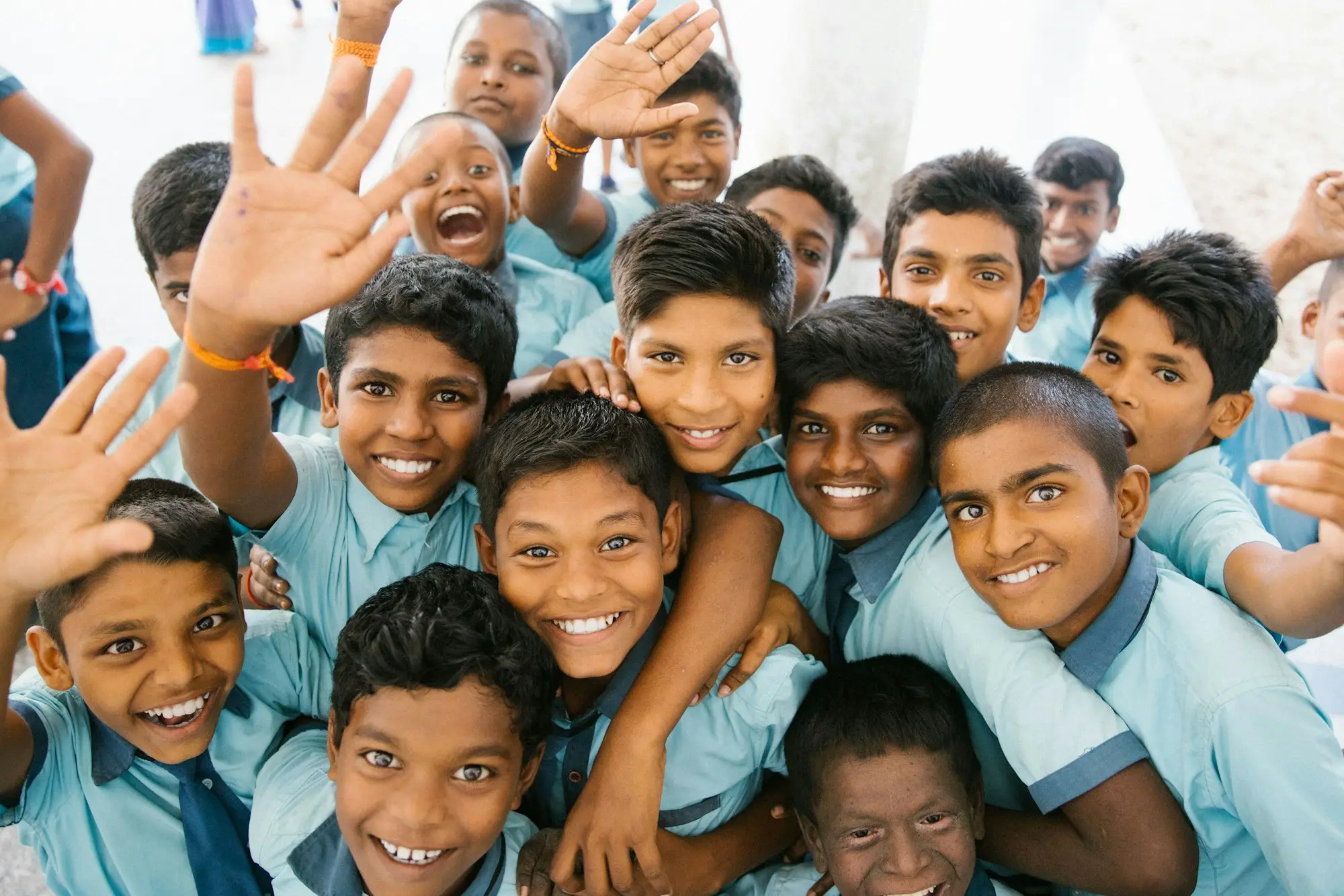 A crowd of schoolchildren in pale blue uniform, laughing, one waving at the camera