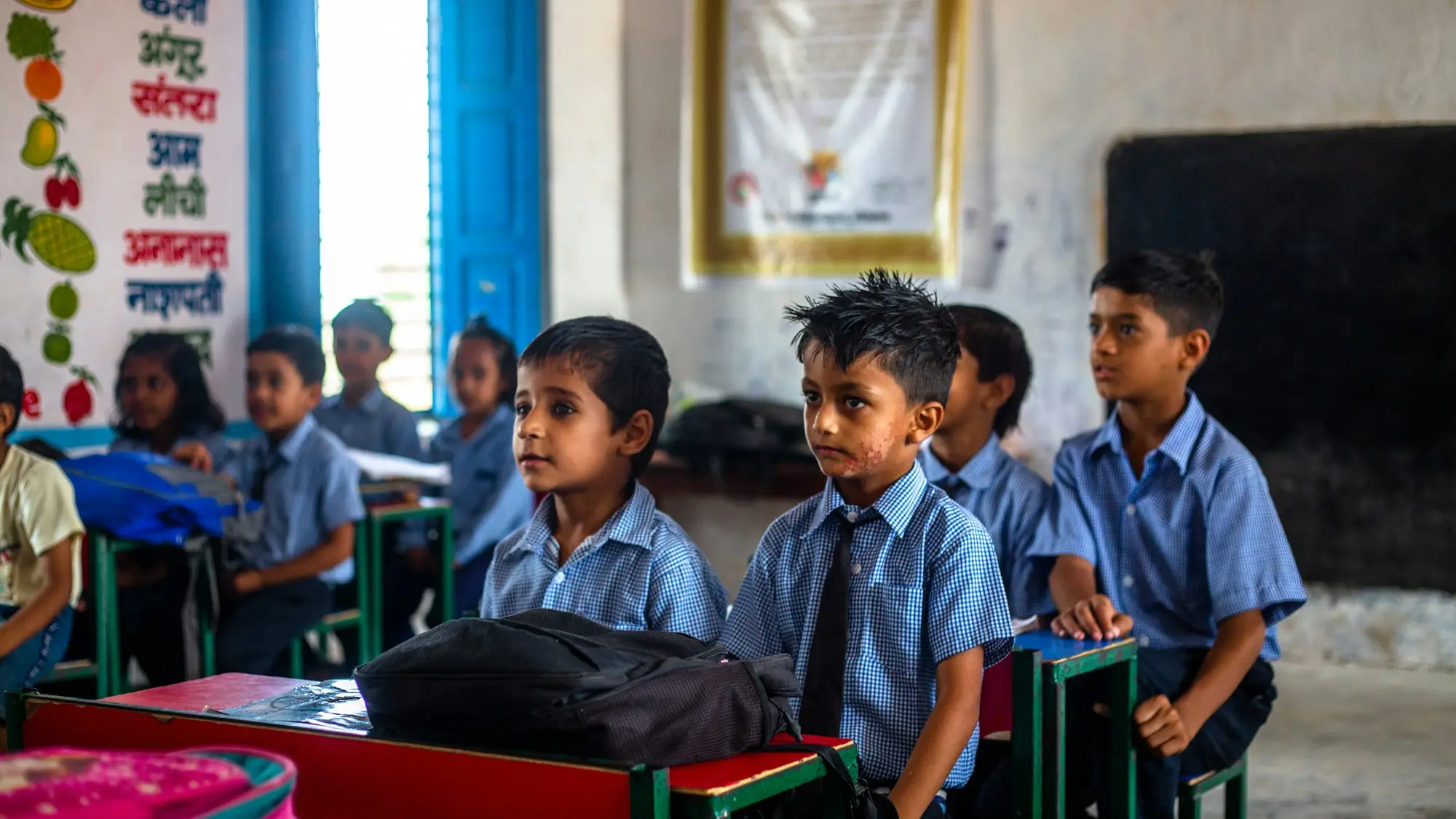 Young children seated at desks in a classroom with blue walls