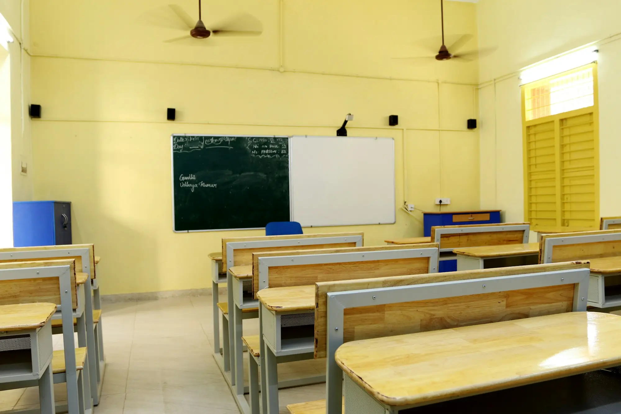 An empty classroom with wooden benches, a blackboard and yellow walls