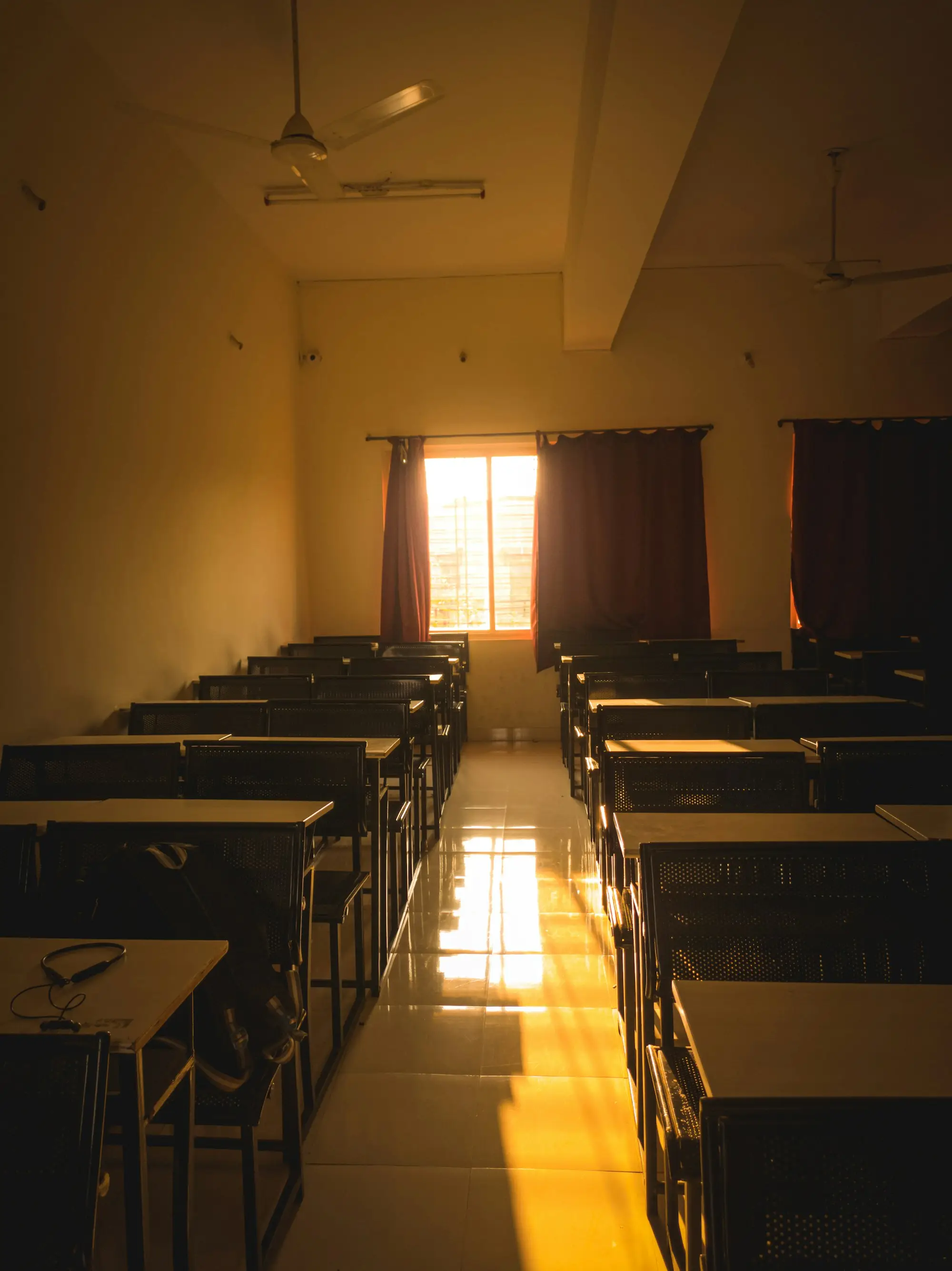 An empty classroom with rows of desks and afternoon light through the window