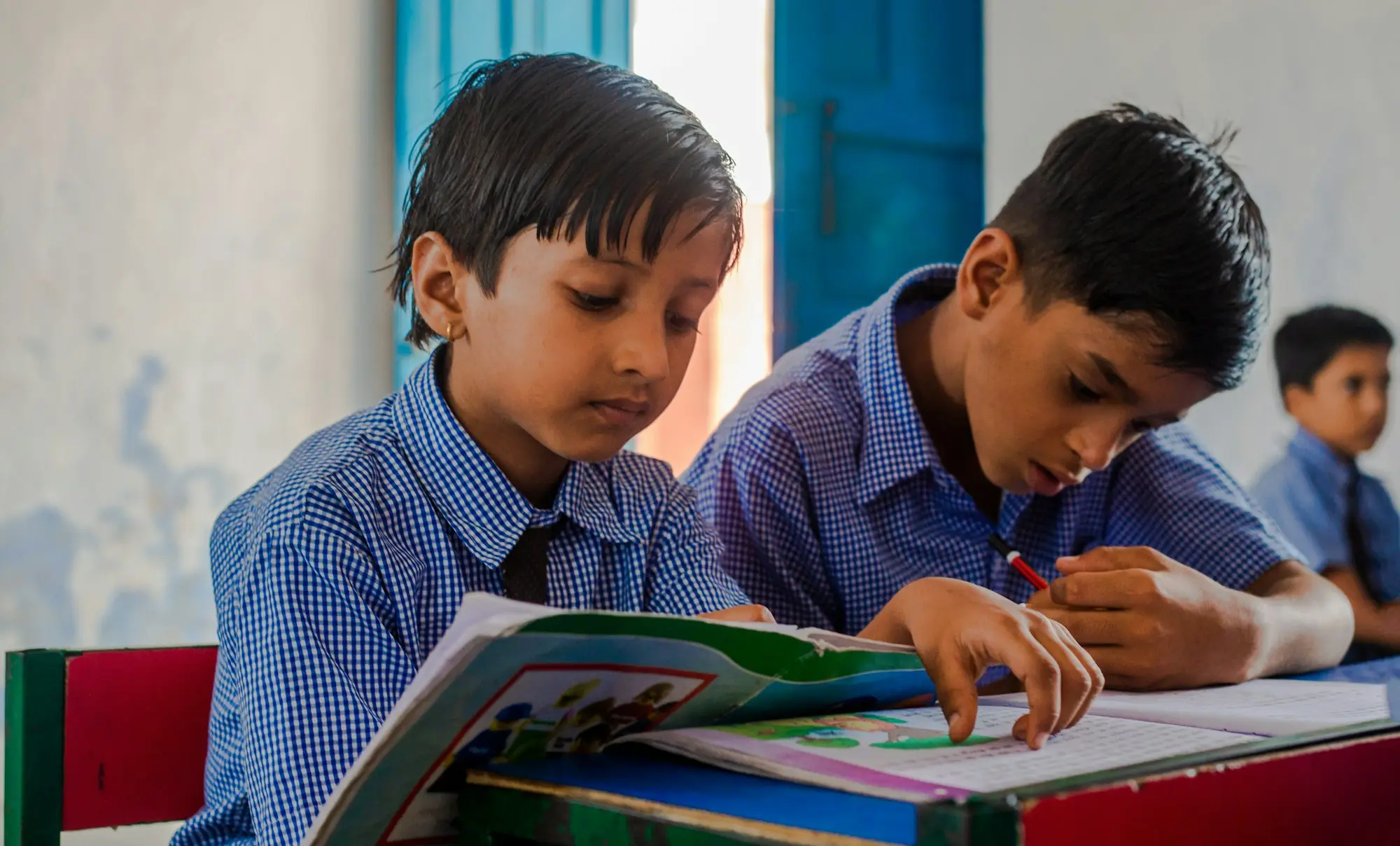 Two boys in checked uniform shirts reading a book together at a desk