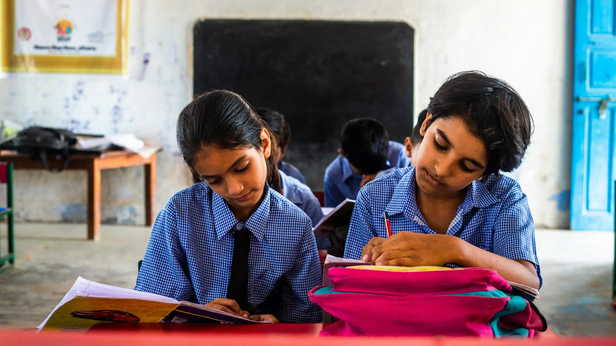 Two girls in school uniform working through books at a classroom desk