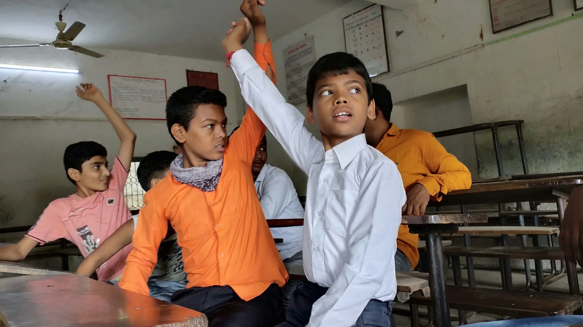 Two boys in a classroom, one with his hand raised